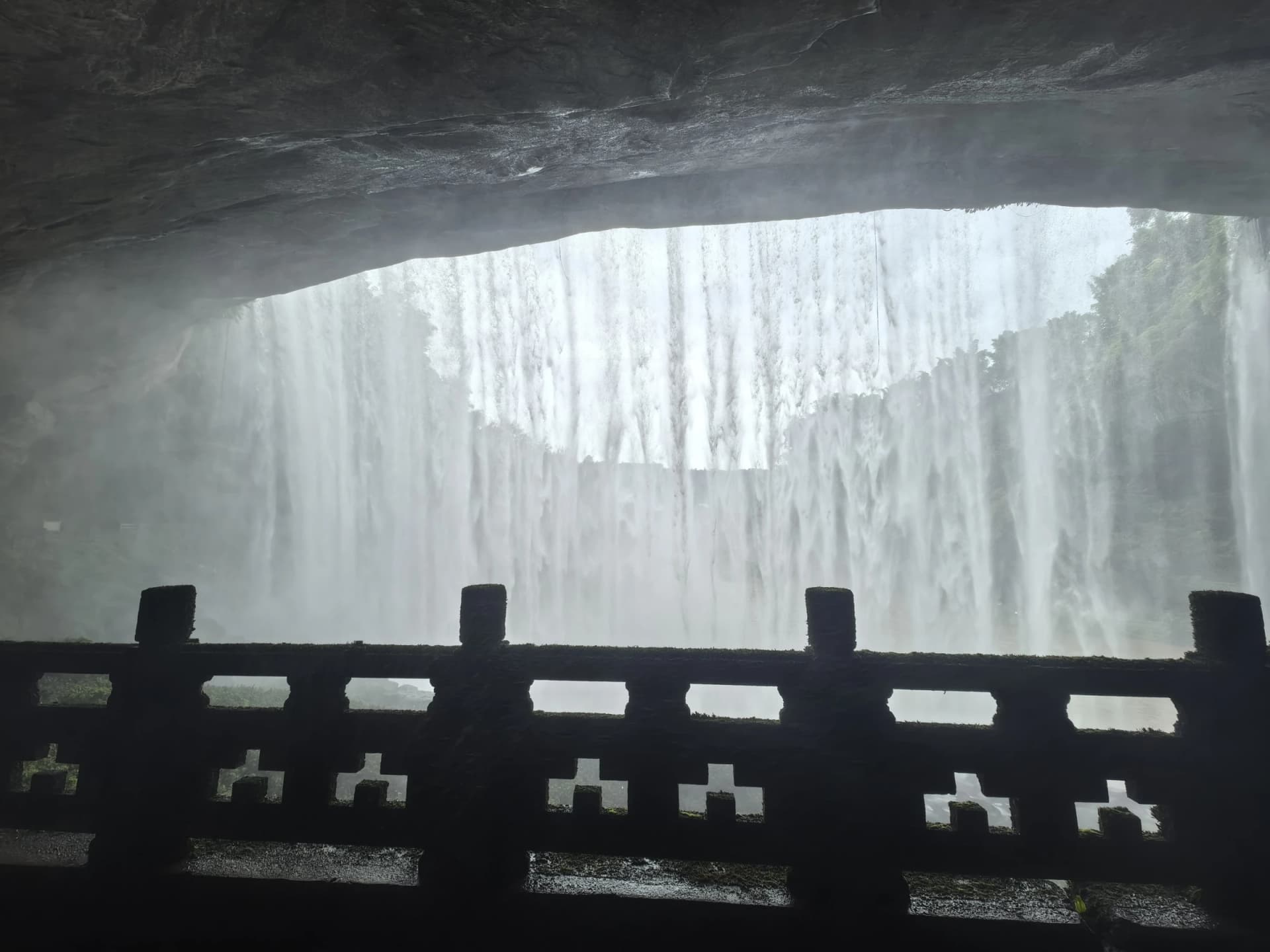 Tirai air Air Terjun Wanzhou dilihat dari bawah ceruk batu yang gelap di belakang pagar pada Oktober 2025.