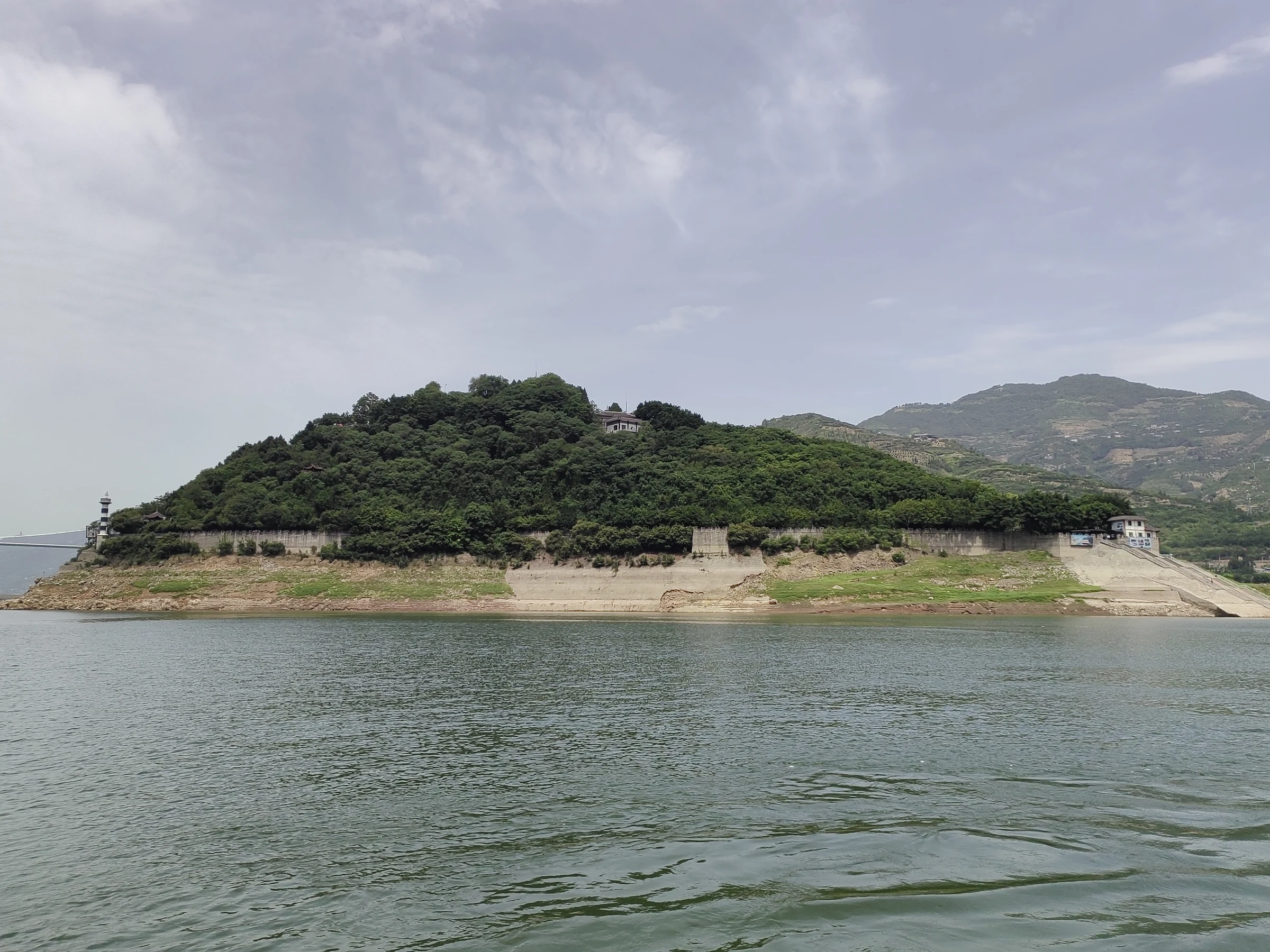 Gunung Baidi menjulang di atas air waduk di bawah langit mendung pada Mei 2025.